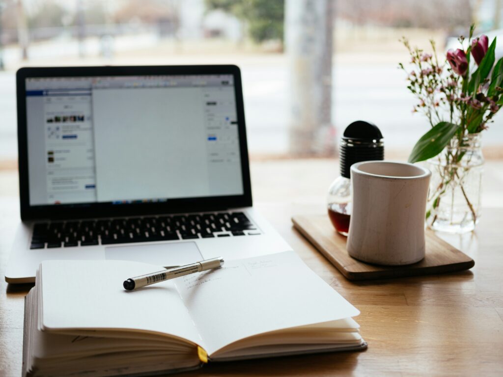 Imagen que llama a la creatividad mostrando una notebook, una taza y un cuaderno con una birome encima.